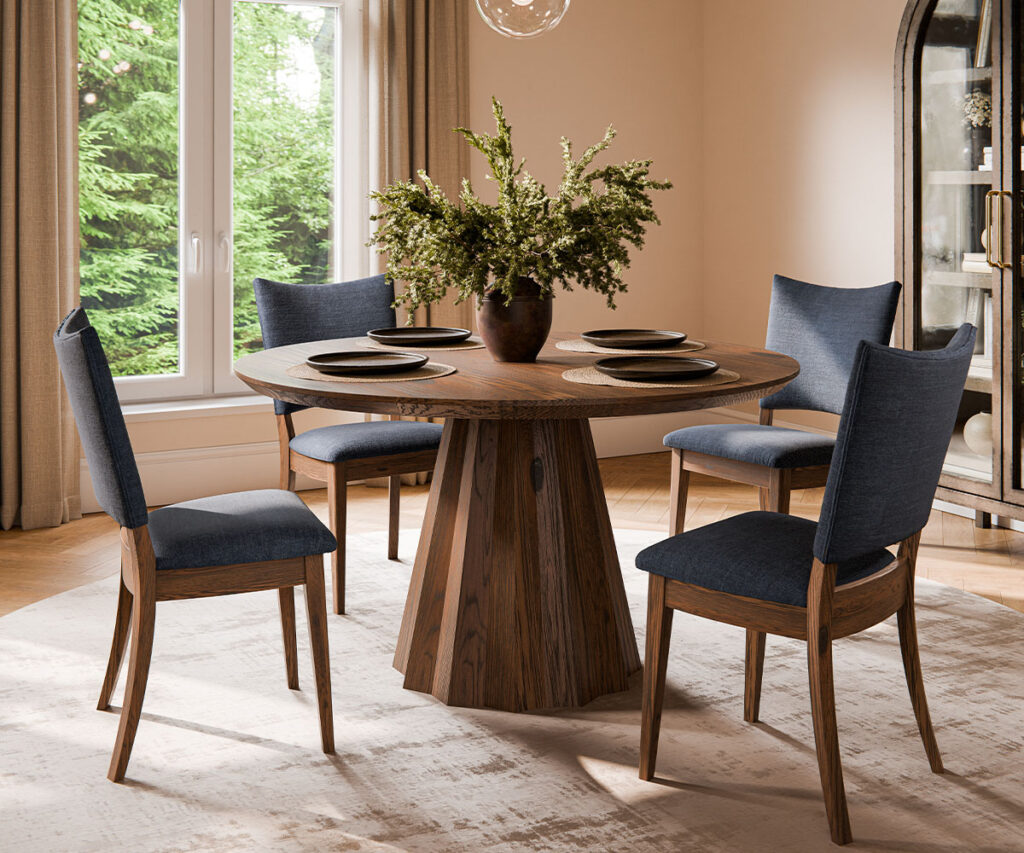 Round pedestal dining table with blue upholstered chairs in a light-filled room.