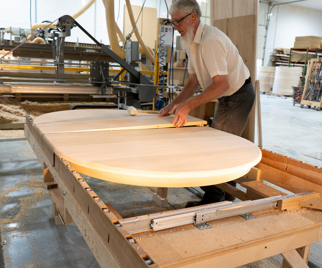 Amish craftsman shaping solid wood tabletop in workshop